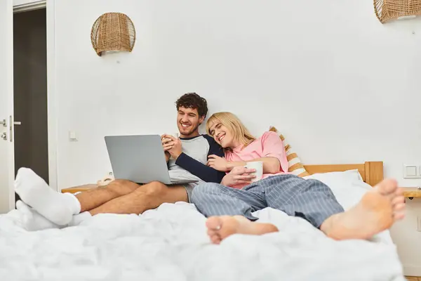 Due uomini condividono un pomeriggio gioioso sul letto, ridendo e utilizzando un computer portatile mentre si rilassano insieme. — Foto stock