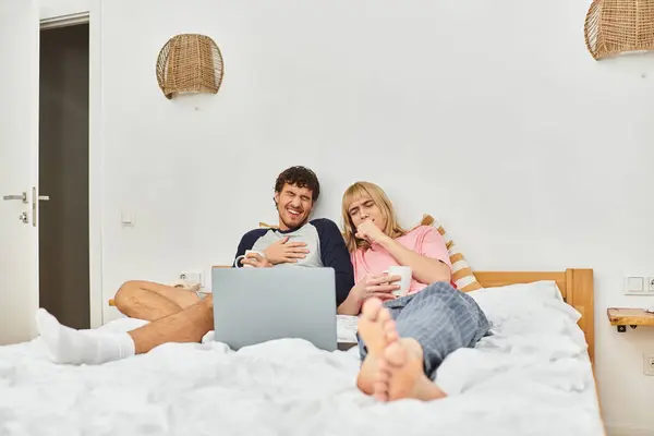 Dois homens relaxam em uma cama, compartilhando risos e lanches enquanto assistem a um filme em seu espaço acolhedor. — Fotografia de Stock