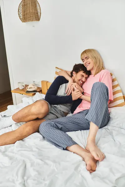 Two men share a warm embrace on a comfortable bed, radiating love and joy in their cozy space. — Stock Photo
