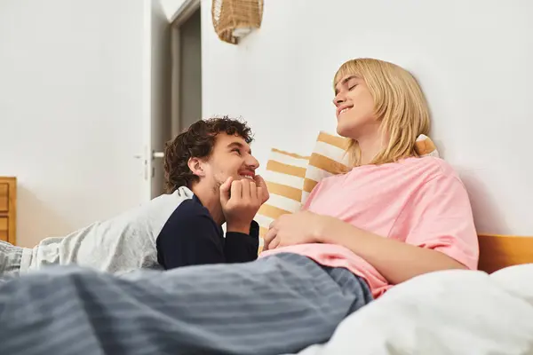 Deux hommes rient et partagent des regards tendres tout en se relaxant ensemble sur une literie douce. — Photo de stock