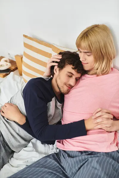 Two men share a tender moment while lying in bed, wrapped in each others arms and smiles. — Stock Photo