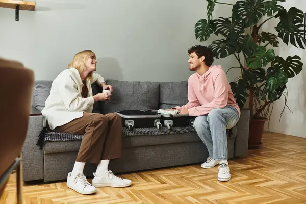 Two joyful men share laughter and love as they pack their suitcase on a comfortable couch. — Stock Photo