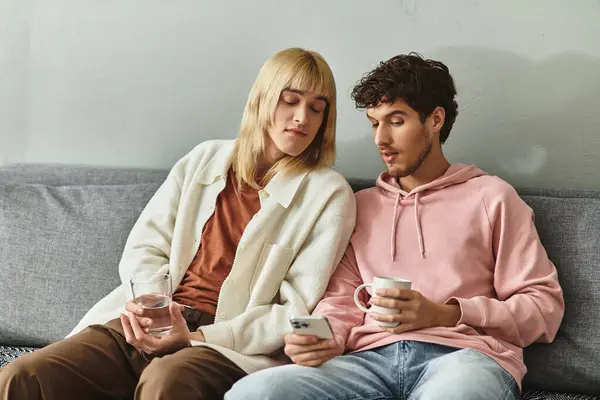 Two men share a tender moment on a couch, engaging with a mobile device while sipping drinks. — Stock Photo