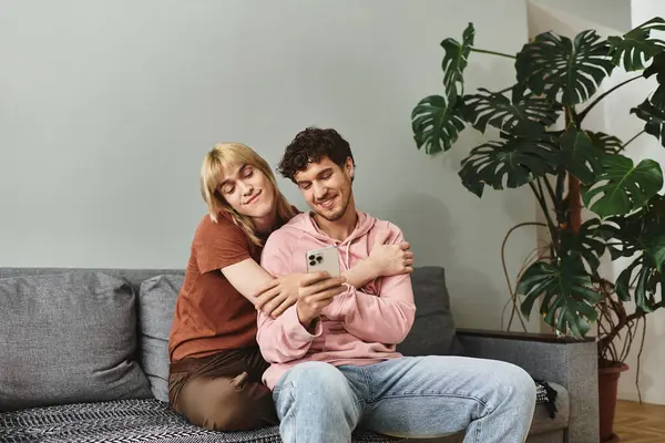 Ein Paar entspannt sich zusammen auf einer bequemen Couch und lächelt beim Anblick eines Telefons. — Stockfoto