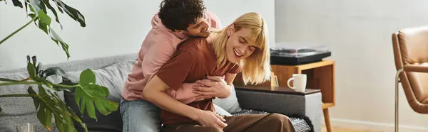 Deux hommes s'embrassent joyeusement sur un canapé dans un salon chaleureux rempli d'amour et de rire. — Photo de stock