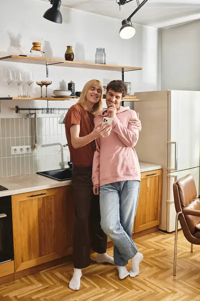 Two men share smiles while looking at a phone in a modern kitchen filled with warmth. — Stock Photo