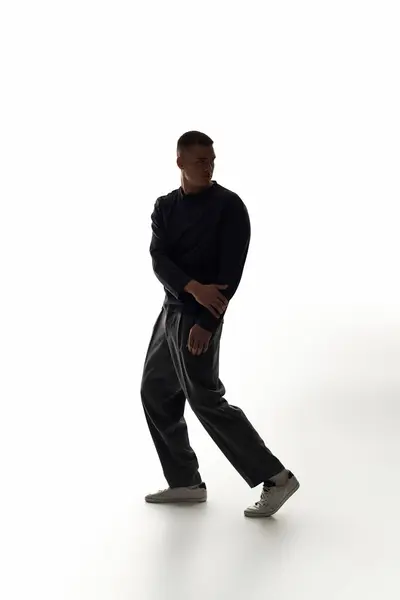 Ein junger Mann nimmt eine dramatische Pose ein und präsentiert seinen Stil und sein Selbstvertrauen in einem hellen Raum. — Stockfoto