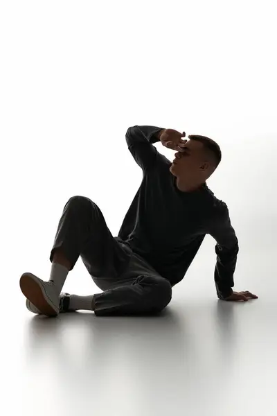 A young man strikes a thoughtful pose on the floor, highlighting his style against a light backdrop. — Stock Photo