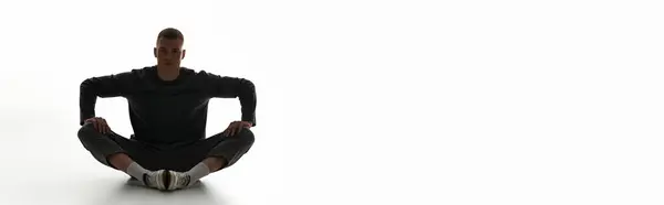 A handsome young man sits in a relaxed pose, showcasing calm confidence in a spacious studio. — Stock Photo