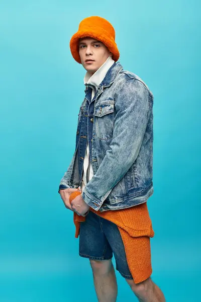 A young man showcases a trendy denim jacket and orange hat, radiating confidence and style. — Stock Photo