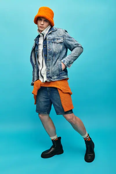 Young man poses stylishly in denim with bright orange accents against a blue background. — Stock Photo
