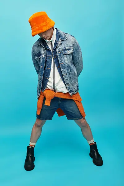 A young man stands confidently, wearing a denim jacket and bucket hat, with a playful vibe. — Stock Photo