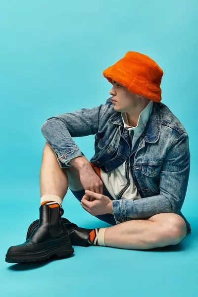 A handsome young man sits comfortably on the floor, showcasing his stylish outfit and vibrant hat. — Stock Photo