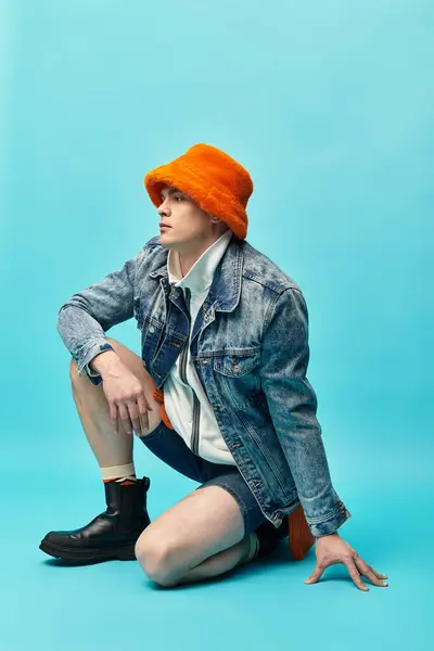 Dressed in a denim jacket and orange bucket hat, a young man crouches gracefully on the floor. — Stock Photo