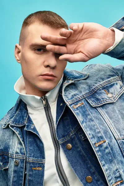 A young man poses confidently, showcasing a stylish denim jacket with a bright background. — Stock Photo