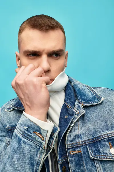 A young man stands confidently, his hand touching his face, showcasing a trendy denim jacket. — Stock Photo