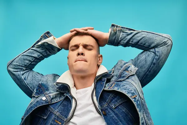 Handsome young man with a trendy denim jacket relaxes against a bright backdrop, expressing joy. — Stock Photo