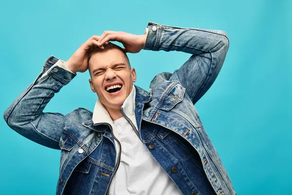 A young man laughs heartily while posing playfully against a vibrant blue backdrop, showcasing joy. — Stock Photo