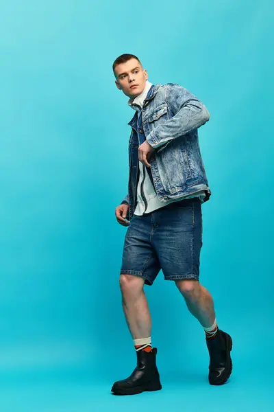 A young man showcasing his trendy denim outfit while exuding confidence in a colorful setting. — Stock Photo