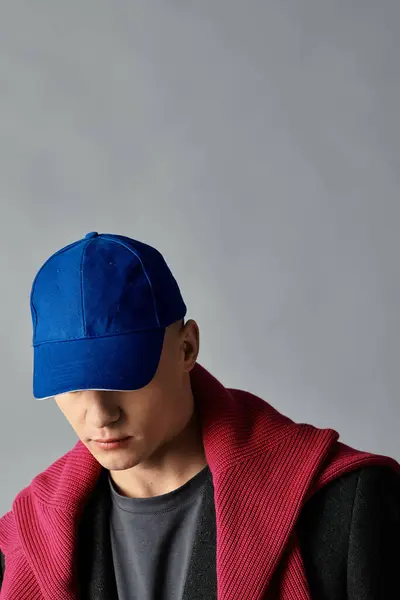 A young man wearing a blue cap and a red sweater rests his head, striking a fashionable stance. — Stock Photo
