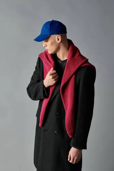 Un jeune homme pose avec confiance dans un manteau noir élégant et une écharpe colorée dans un studio minimaliste. — Photo de stock