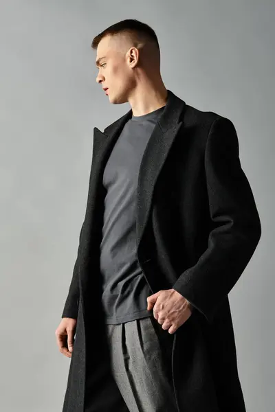 Young man showcases modern fashion in a sleek coat, highlighting elegance and style in a soft light. — Stock Photo