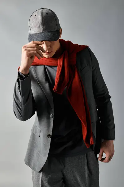 Un jeune homme pose en toute confiance dans une tenue élégante avec un foulard et un bonnet, émanation de style et de charme. — Photo de stock