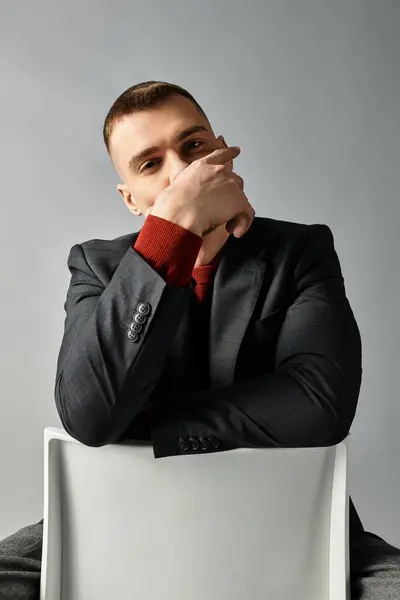 A young, handsome man sits in a stylish chair, resting his chin on his hand with an intriguing gaze. — Stock Photo