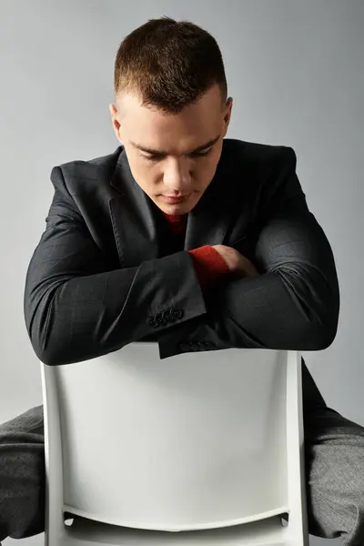 A handsome young man sits calmly on a chair, lost in thought, wearing a smart suit and looking down. — Stock Photo