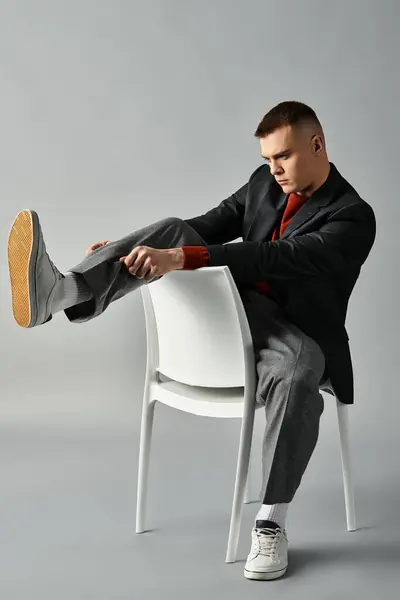 Beau jeune homme assis élégamment sur une chaise, ajustant sa chaussure dans un cadre contemporain. — Photo de stock