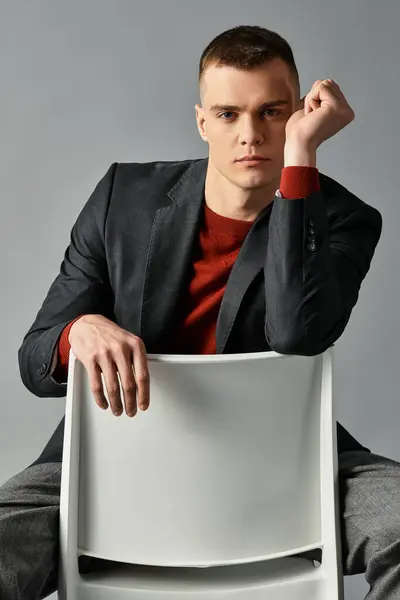 A handsome young man dressed in a tailored suit leans on a chair, lost in contemplation indoors. — Stock Photo
