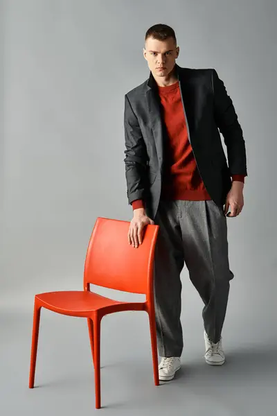 A young, handsome man confidently stands next to a bright red chair in a minimalist space. — Stock Photo
