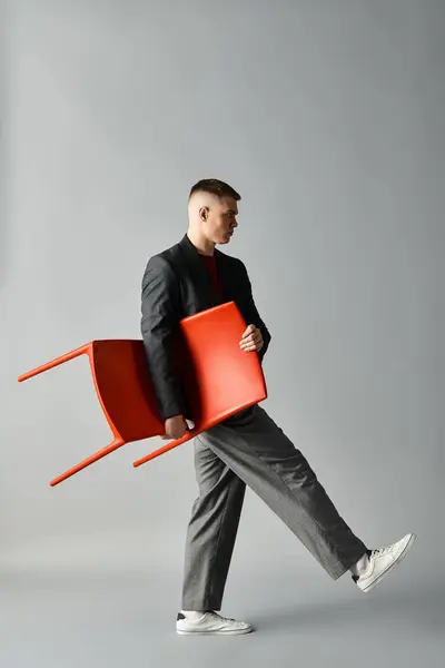 Elegantemente vestito giovane uomo passi con una sedia rossa in un ambiente moderno studio. — Foto stock