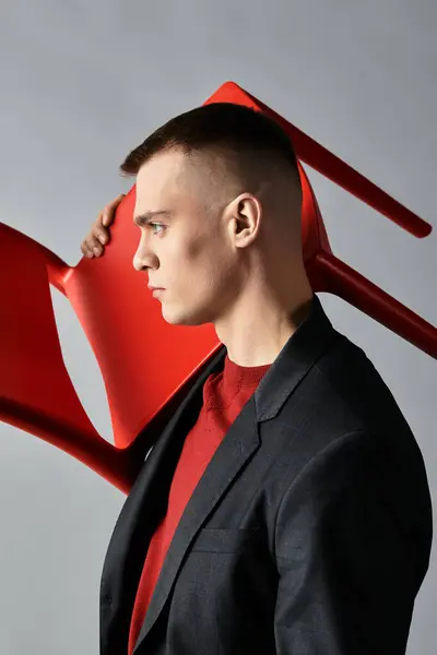 A young man dressed in a suit showcases a modern artistic side while holding a red chair. — Stock Photo