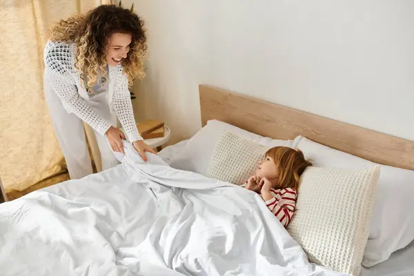 A mother gently tucks her daughter in bed, creating a warm and loving atmosphere at home. — Stock Photo
