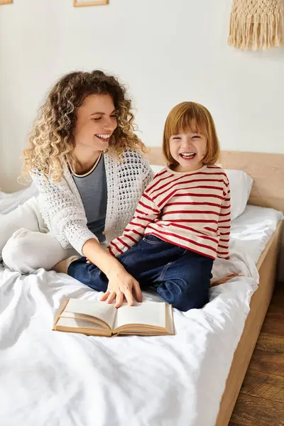 A mother and daughter share laughter while reading together on a cozy bed in a serene room. — Stock Photo