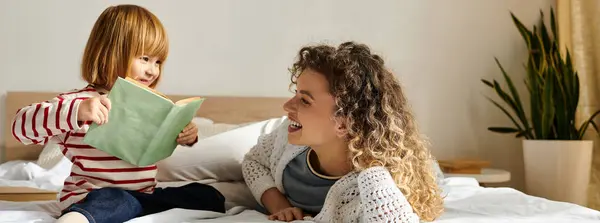 Mother and daughter share a joyful moment while reading on a cozy bed in a bright, modern room, banner — Stock Photo