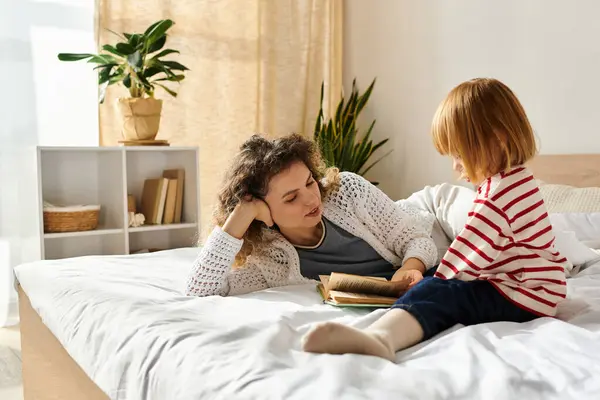 Curly-haired mother and daughter share a cozy moment reading together on a bed at home. — Stock Photo