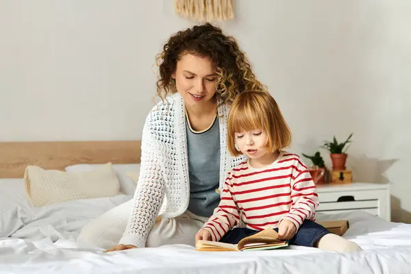 Curly mother and daughter enjoy a quiet afternoon immersed in a book on their comfy bed. — Stock Photo