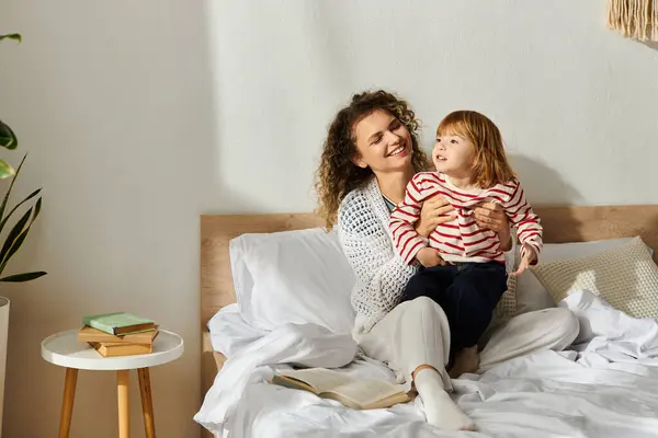 Curly-haired mother cherishes playful moments with her daughter in a warm, inviting bedroom. — Stock Photo