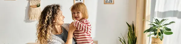 Une mère tient sa fille joyeuse dans un salon lumineux, mettant en valeur leur lien spécial, bannière — Photo de stock