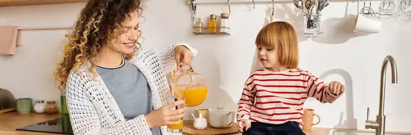 Una madre e una figlia condividono una risata mentre versano succo nella loro luminosa cucina, striscione — Foto stock