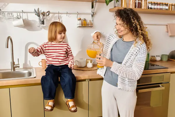 Curly-haired mother shares a delightful drink with her young daughter in a warm kitchen. — Stock Photo