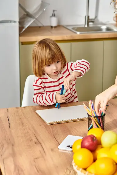 A mother engages with her daughter as they enjoy a creative moment at their kitchen table. — Stock Photo