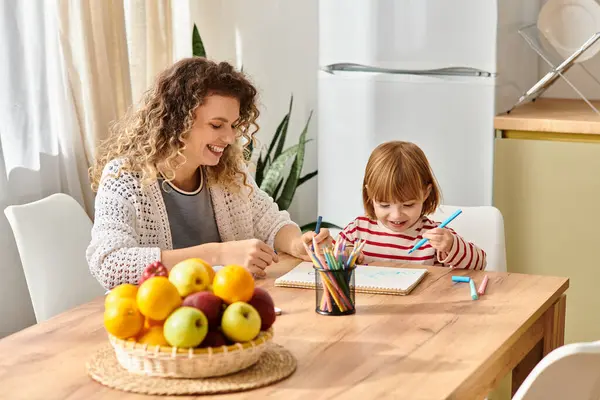 Mãe e filha compartilham um momento alegre desenho e coloração em sua mesa de cozinha. — Fotografia de Stock