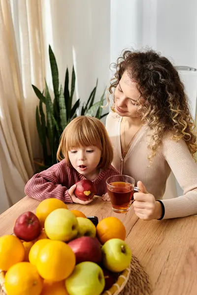 Madre e figlia dai capelli ricci condividono momenti gustando tè e frutta fresca a casa. — Foto stock