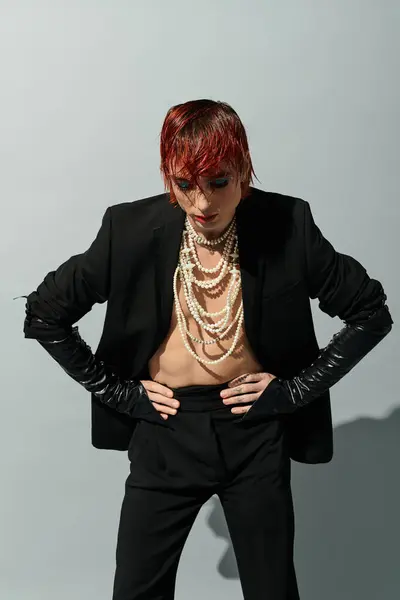 A confident young man poses in a stylish blazer and layered necklaces against a minimal backdrop. — Stock Photo