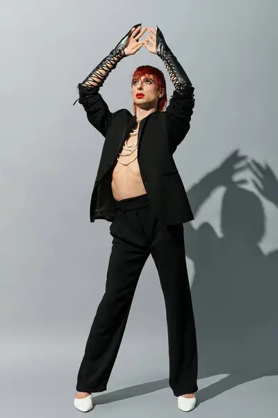 A young man confidently poses in a stylish black outfit against a gray backdrop. — Stock Photo