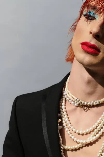 A young man showcases vibrant makeup and layered pearl necklaces against a gray backdrop. — Foto stock