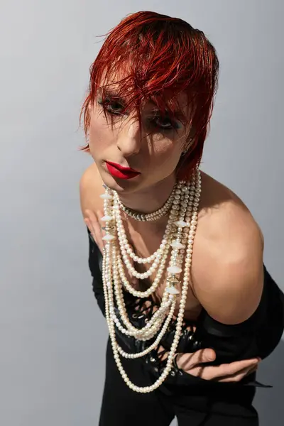 A unique young man flaunts bold red hair and layered pearl necklaces against a plain background. — Stock Photo